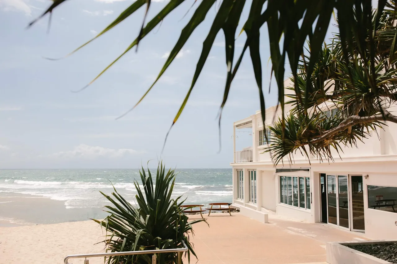 A beachfront building framed by pandanus palms on a sunny day by the surf