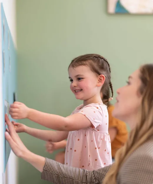 A young girl playing at a wall panel beside a therapist, from Northside Speech Pathology