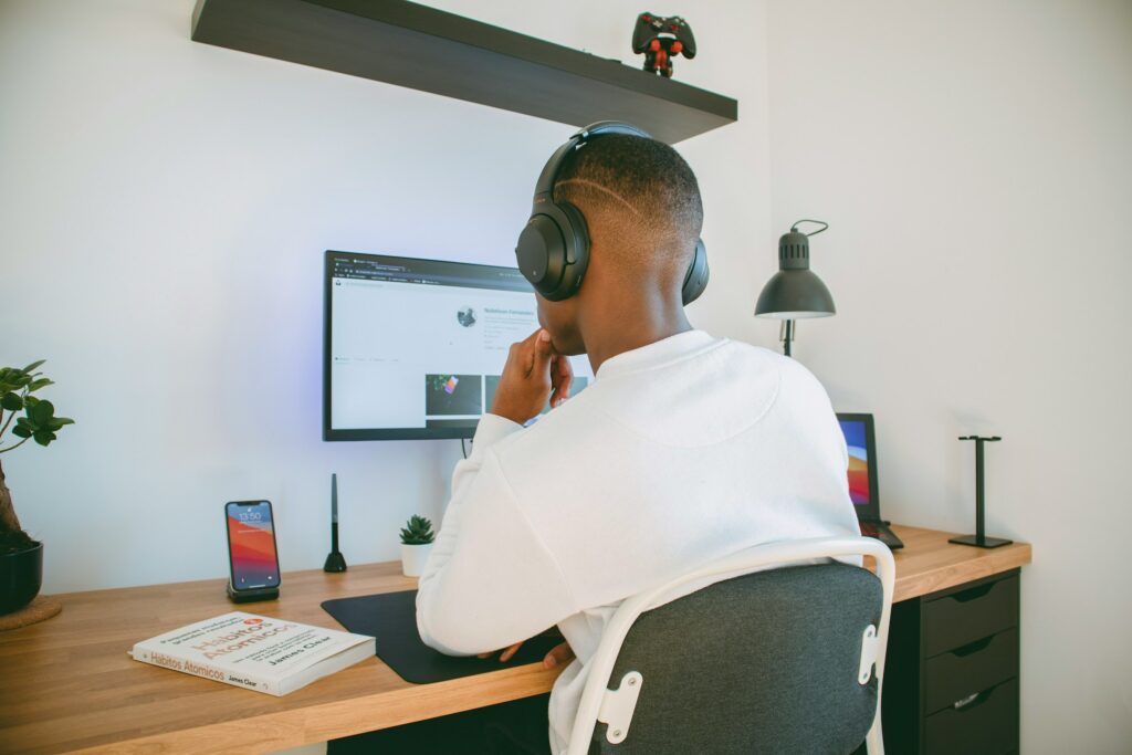 A Man Wearing Headphones Is Sitting At A Desk In His Home Office, In Front Of A Computer.