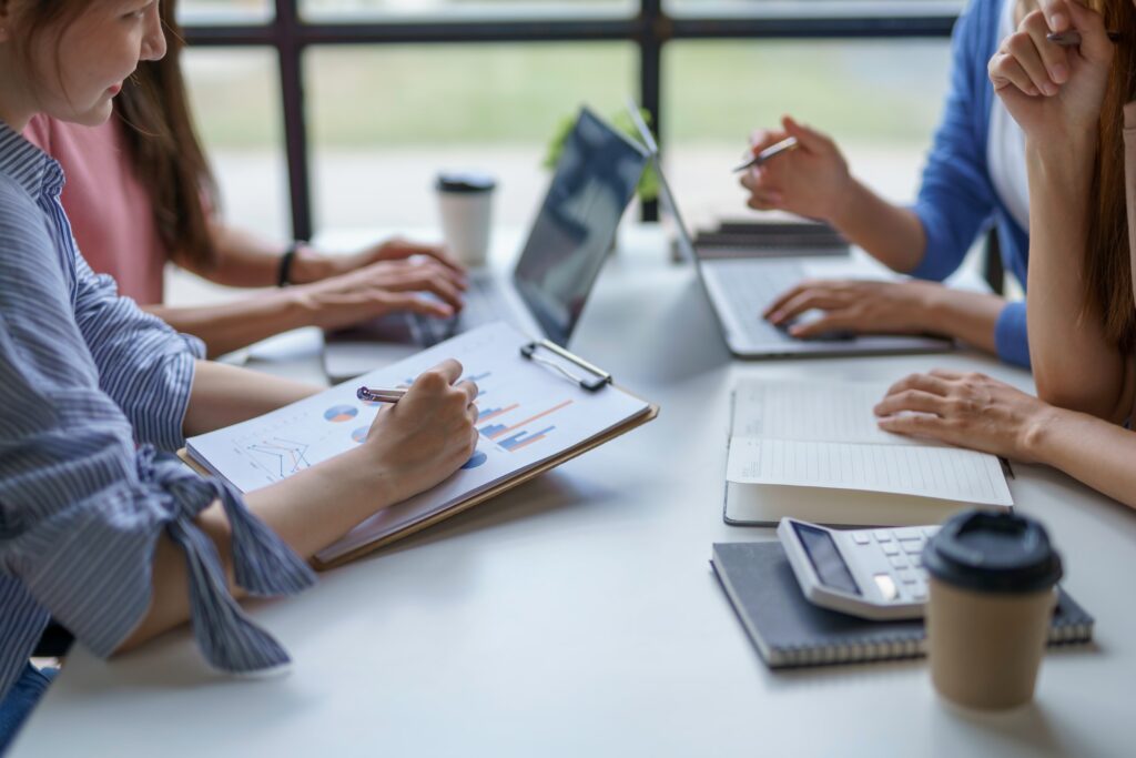 A group of people sitting around a table working on their laptops and discussing project management salaries.