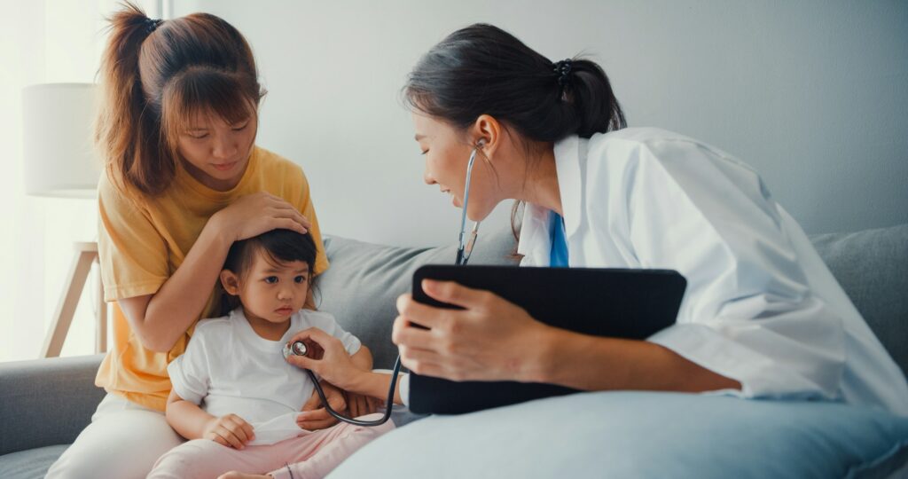 A Woman In Australia Is Holding A Stethoscope While A Child Is Sitting On The Couch.