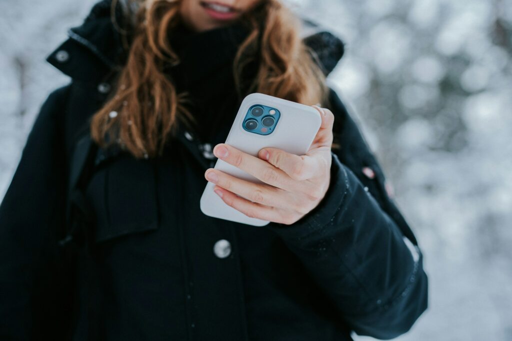 A woman holding an iPhone in the snow.
