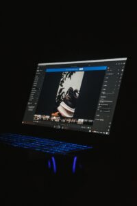 A laptop screen showcasing photo editing software with an image of a shoe in view highlights the process of applying presets to enhance multiple photos in Lightroom. The keyboard emits a cool blue light, contrasting against the dark background.