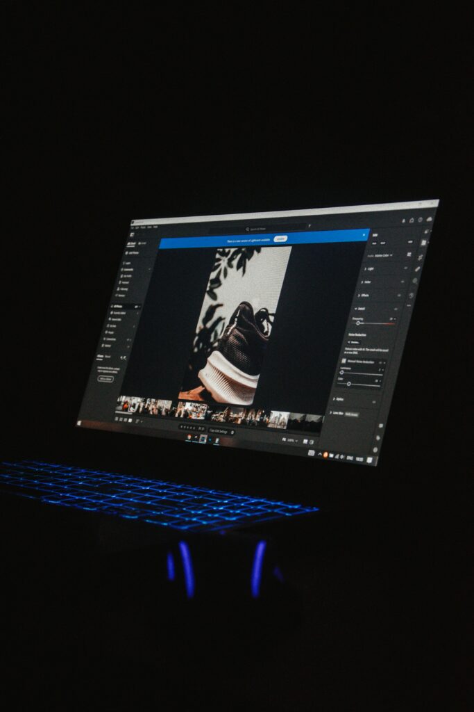 A laptop screen showcasing photo editing software with an image of a shoe in view highlights the process of applying presets to enhance multiple photos in Lightroom. The keyboard emits a cool blue light, contrasting against the dark background.