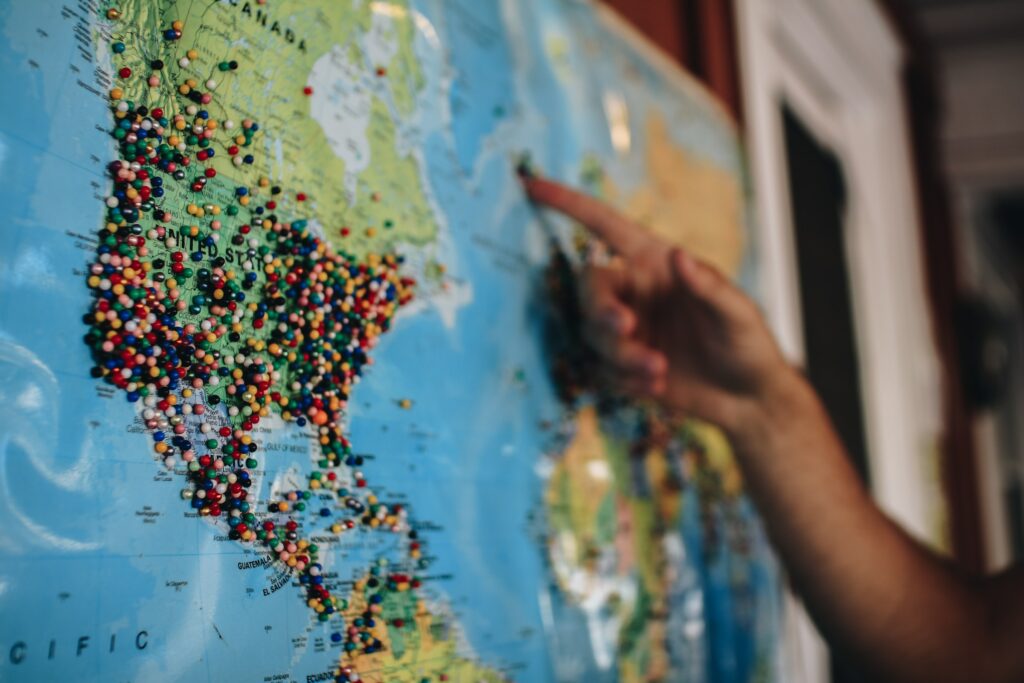 A brutally honest travel agent pointing at a map with pins on it.