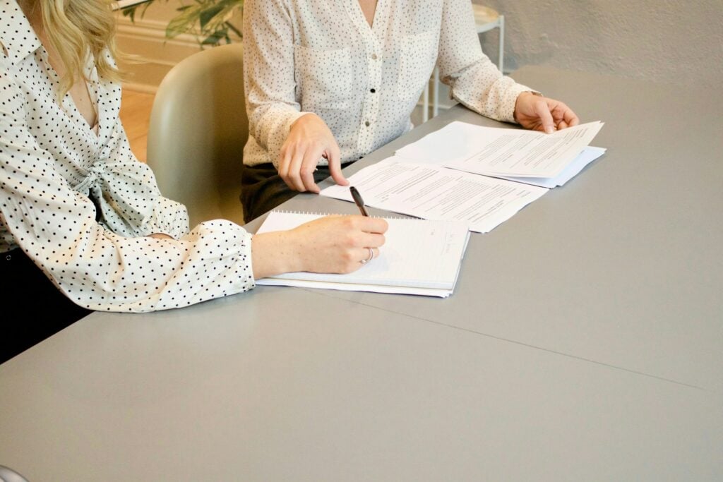 Two individuals reviewing and signing documents related to "How to Become an Intellectual Property Paralegal" at a table.