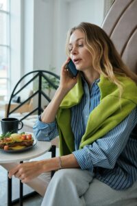 A woman sitting at a table talking on a cell phone, figuring out how to block spam calls on her iPhone.