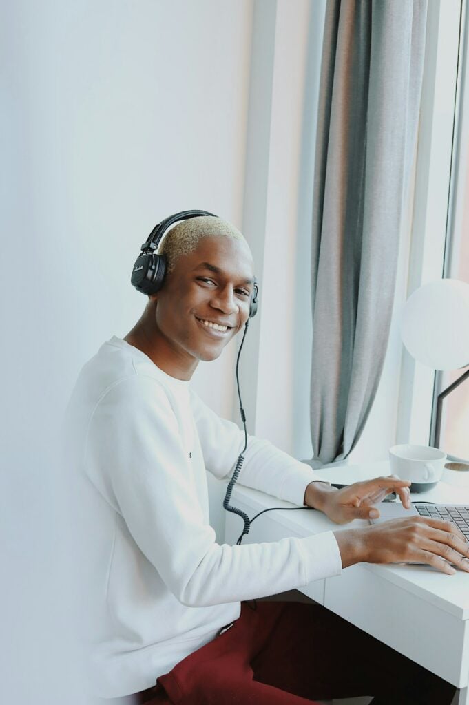 A young man wearing headphones is sitting at a desk with a laptop, engrossed in his Audible membership.