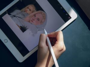 A person is holding an iPad and drawing on it with an Apple Pencil.