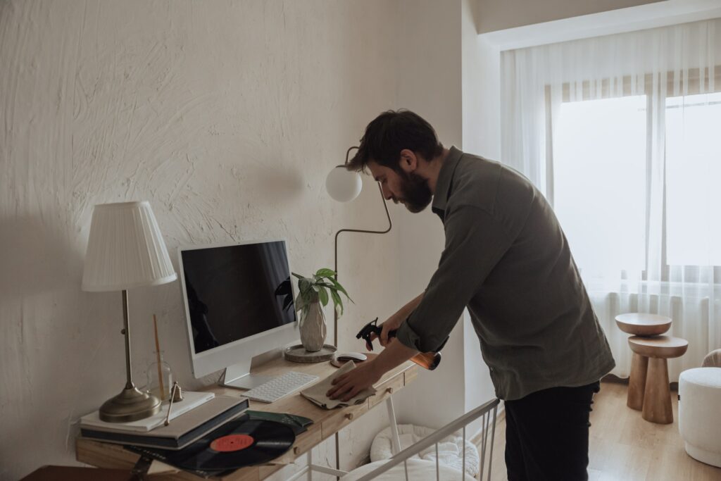 A man working on a computer in his home office while ensuring a hygienic typing experience by cleaning his keyboard.