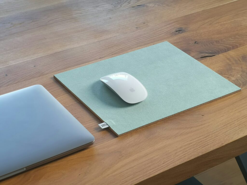 A wireless mouse on a clean mouse pad beside a closed laptop on a wooden table.
