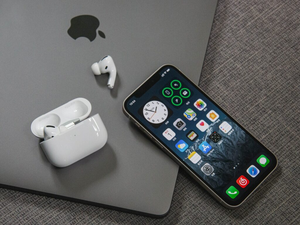 A pair of Apple AirPods sitting next to a laptop while an iPhone is being used to clear cache and free up space.