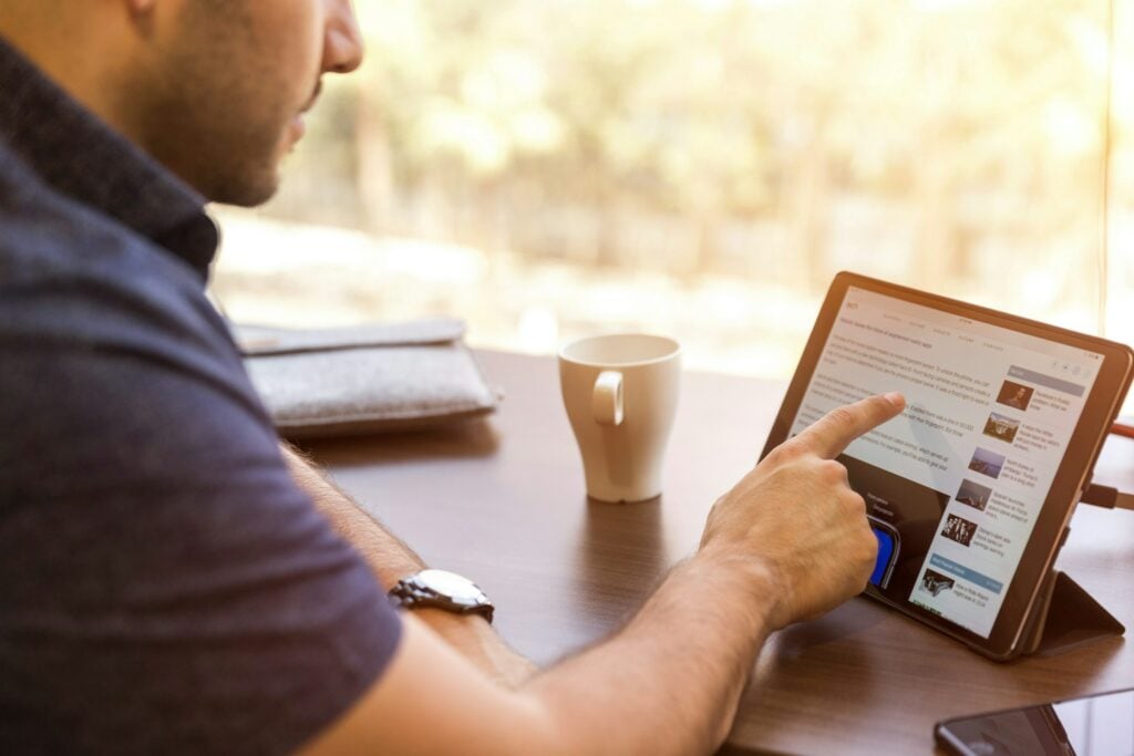 A man is sitting at a desk with an iPad in front of him, browsing the internet using Firefox for a cleaner browsing experience.
