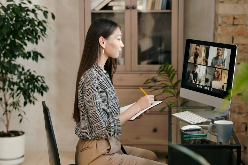 A woman sitting at a desk with a computer and a notepad, expertly navigating through Microsoft Teams to clear cache.