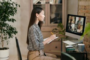 A woman sitting at a desk with a computer and a notepad, expertly navigating through Microsoft Teams to clear cache.