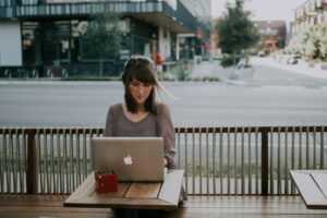 A woman sitting on a bench with a laptop and a cup of coffee while using Firefox.
