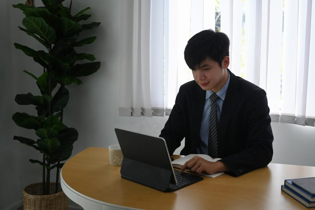 A man in a suit sitting at a desk with a laptop, searching for How to Find Tax File Number.