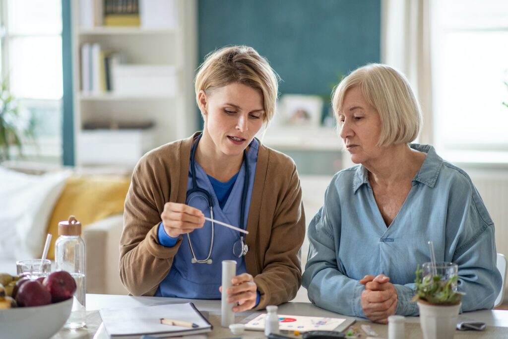 A nurse and an older woman are collaborating at a table while referencing a Complete Guide for NDIS Certificate procedures.