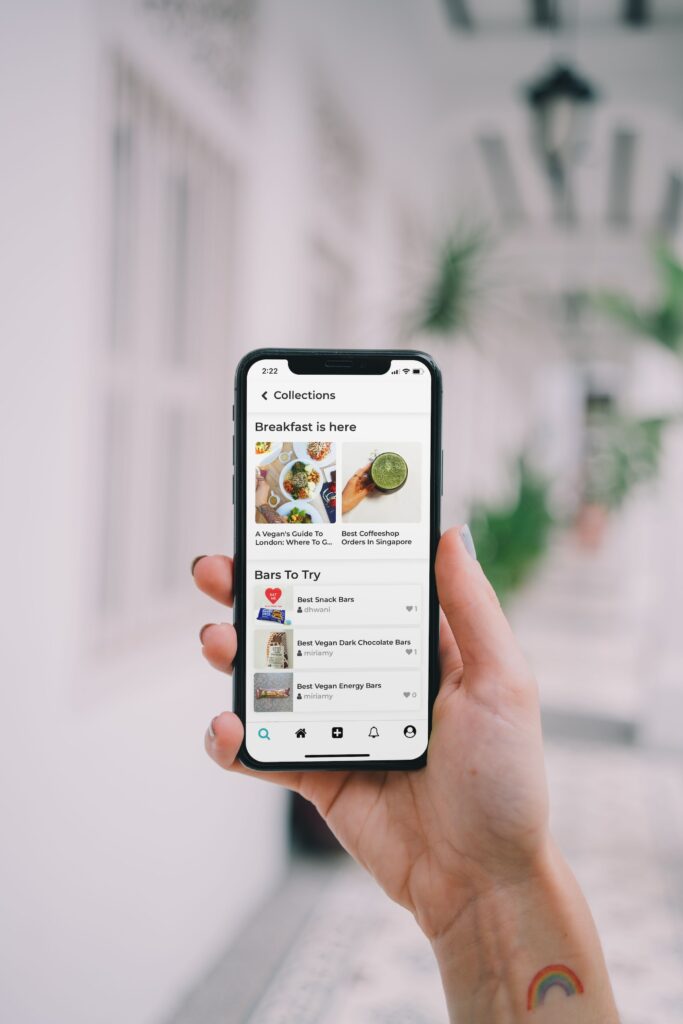 A person holding up an iPhone with a food app on it, taking photos of delicious dishes available to order.