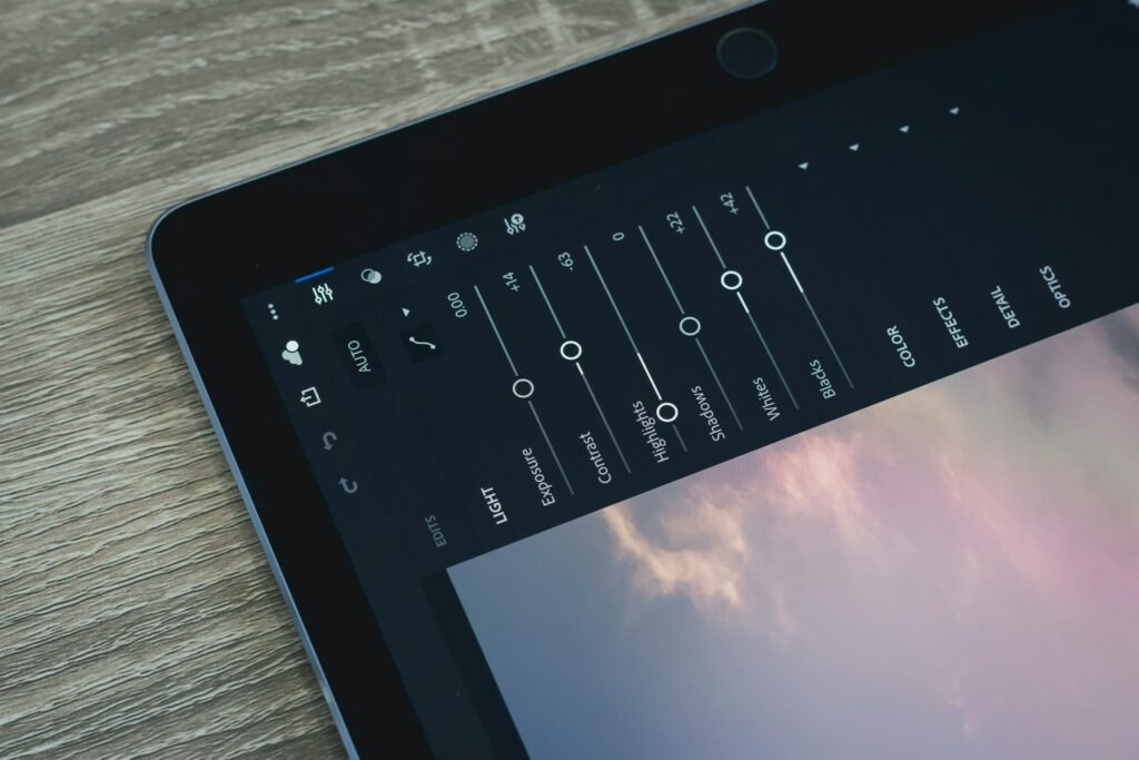 A close-up of a tablet screen shows photo editing tools, with sliders for adjusting light, color, and effects on a wooden surface. Discover the magic of enhancing your images with ease by learning how to install Lightroom presets.