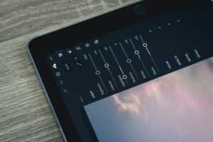 A close-up of a tablet screen shows photo editing tools, with sliders for adjusting light, color, and effects on a wooden surface. Discover the magic of enhancing your images with ease by learning how to install Lightroom presets.