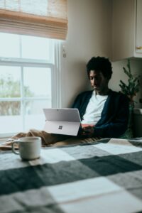 A man sitting on a bed with a laptop by a window, working on making one page landscape in Word.