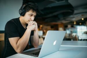 A young man wearing headphones is sitting at a table with a laptop, working on Excel spreadsheets.
