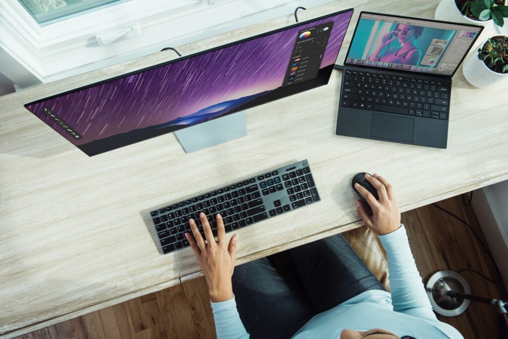 A woman protecting a folder on her desk, with two monitors and a keyboard.