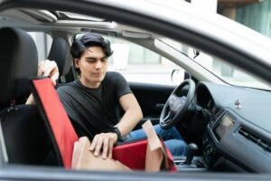 A man in the back seat of a car checks his phone for a guide on how to sell his car in QLD.