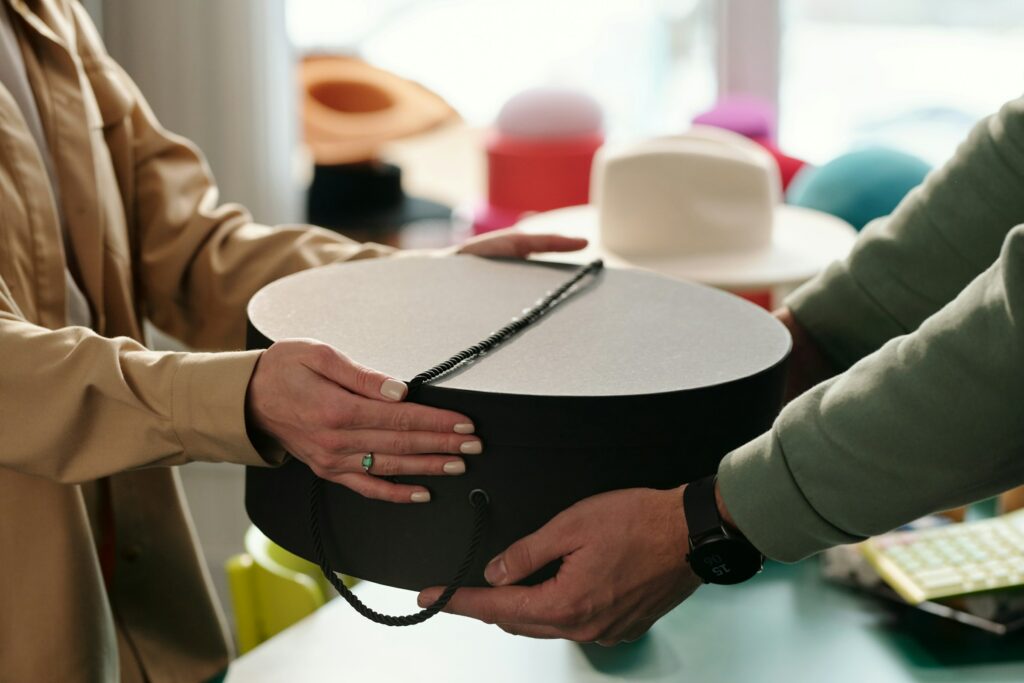 Two People Mastering The Art Of Selling By Handing A Box Of Hats To Each Other.