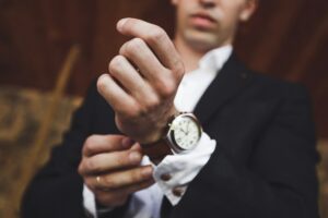 A man adjusting the cuff of his shirt, wearing a dark suit and a watch, ponders, "Is Jomashop legit?