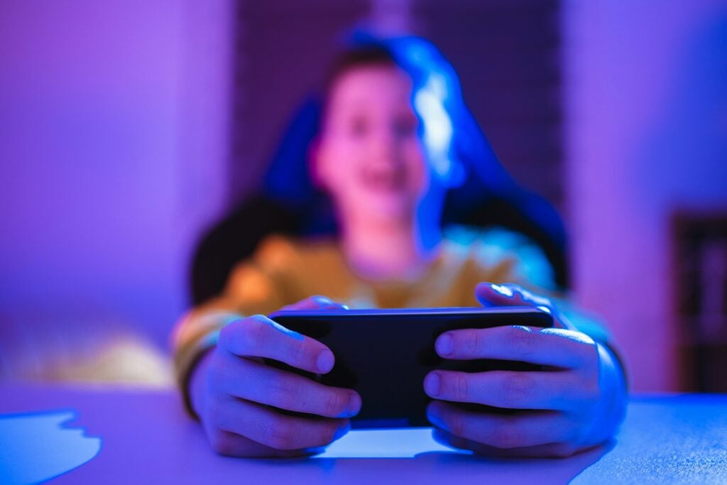 A kid is holding a cell phone in front of a blue light.