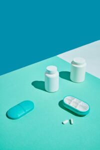 Two white pill bottles, a pill organizer, and scattered pills are arranged on a teal surface with a blue background. If you've ever wondered, "Is Swisse a good brand?" this composition invites curiosity about quality health choices.