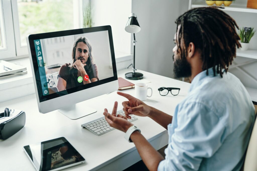 A man participates in an online networking video call with another individual on a desktop computer.