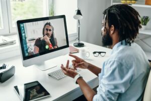 A man participates in an online networking video call with another individual on a desktop computer.