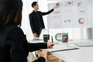 Asian businesswoman pointing at a whiteboard explaining "What Is Scope in Project Management" in an office.