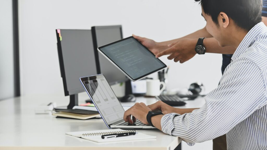 Two people working on a laptop in an office, focused and engaged in their technology jobs.