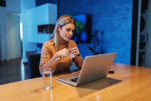 A woman sitting at a table with a laptop, researching Enterprise Content Management, and a cup of coffee.