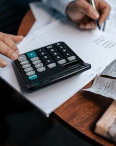 A businessman is using a calculator to guide his calculations while sitting at a table.