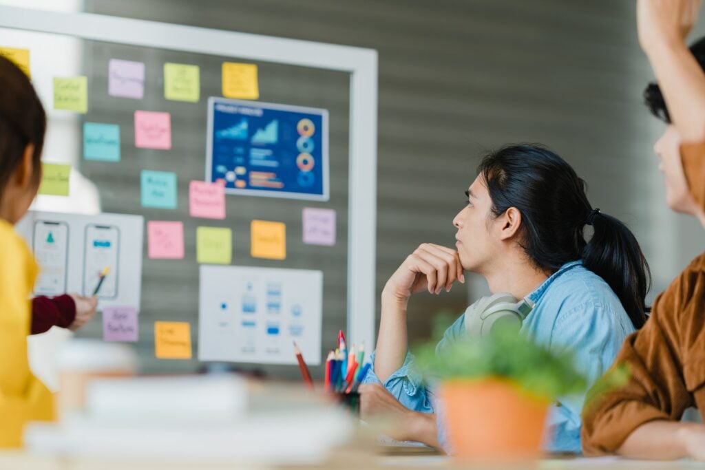 A group of people engaging in a deep dive into the art of learning, sitting at a table with sticky notes on the wall to aid in skill acquisition.