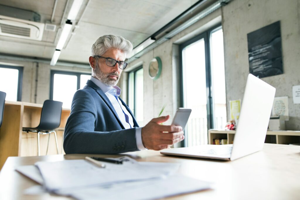 A businessman using a laptop and cell phone in an office while referencing a Comprehensive Guide.