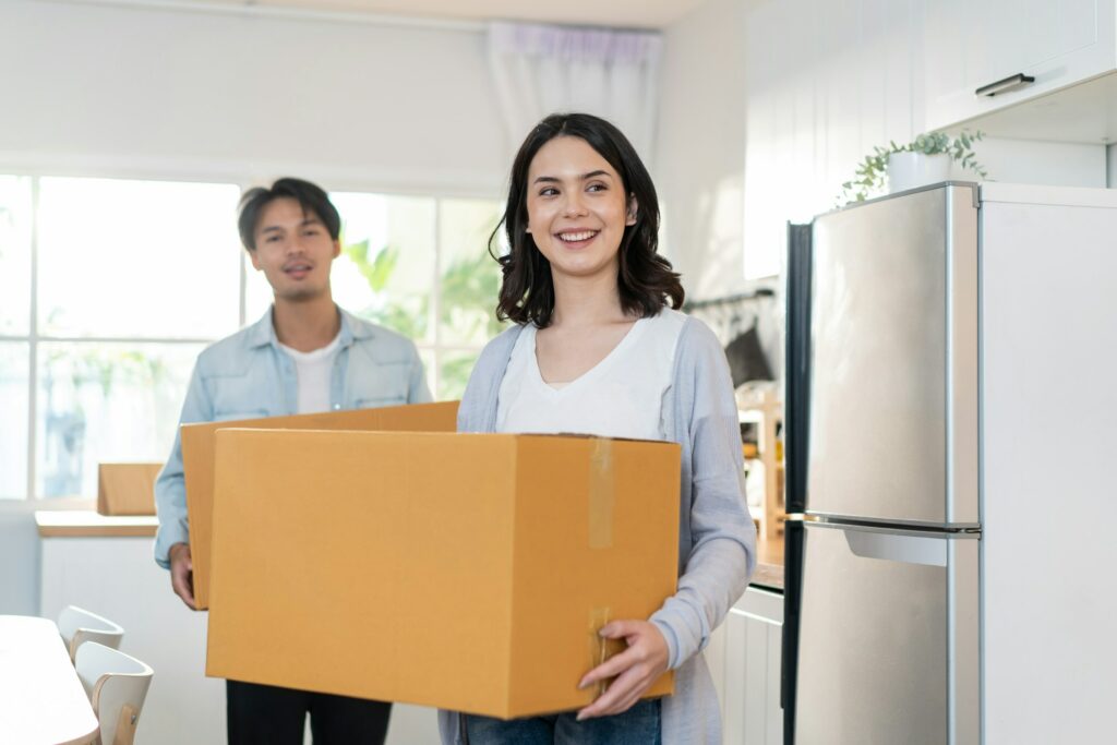 Rental Yield: Young Asian Couple Holding Moving Boxes In The Kitchen.