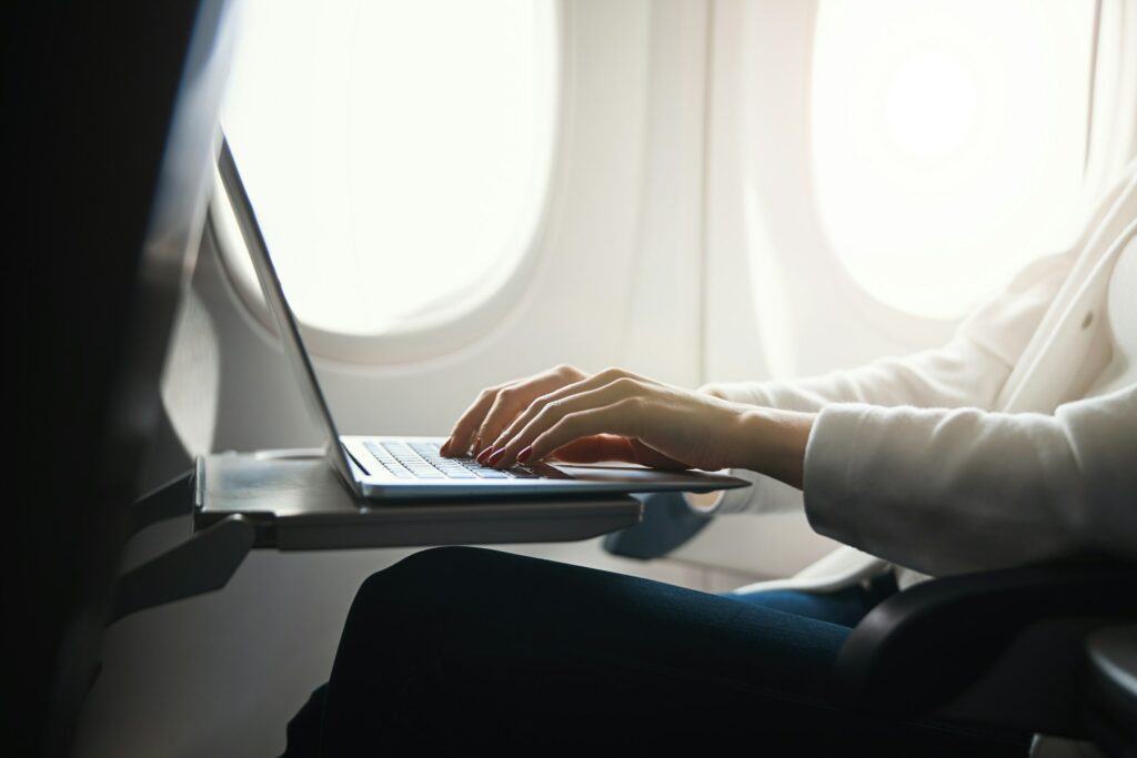 A person using a laptop on the tray table of an airplane seat, with sunlight shining through the window, searches for information on what is a lead generation bot.