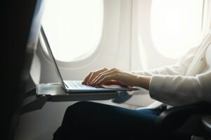 A person using a laptop on the tray table of an airplane seat, with sunlight shining through the window, searches for information on what is a lead generation bot.