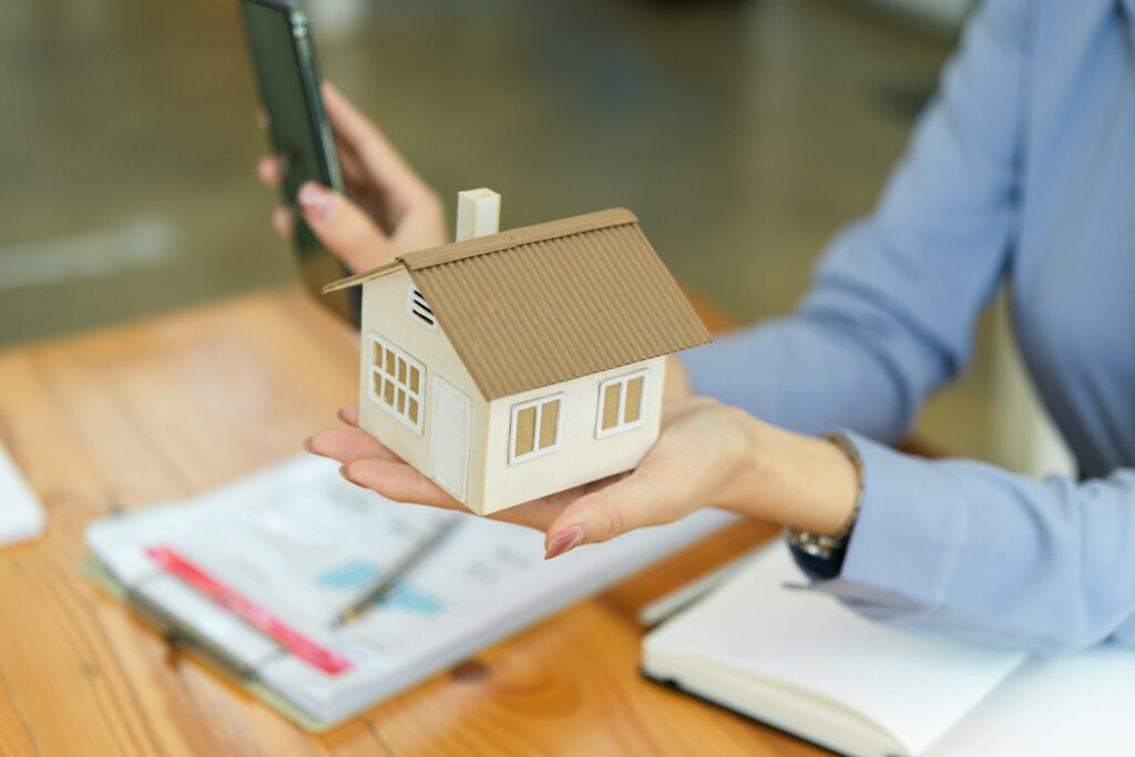 A Woman Holding A Model Of A House And Talking On Her Cell Phone.