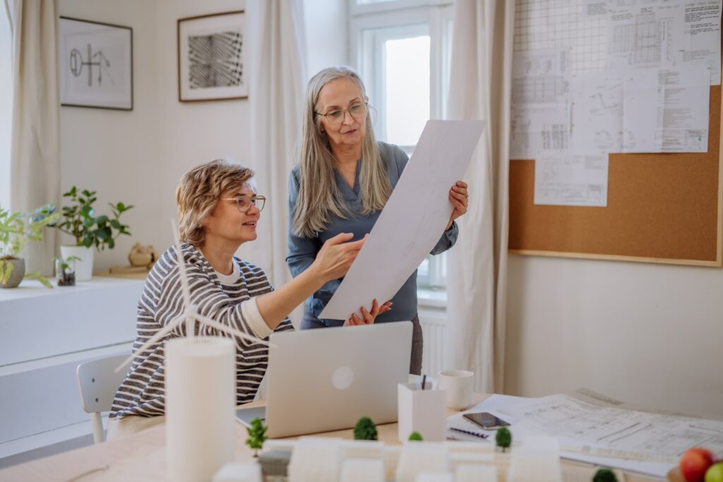 Two women analyzing blueprints in an office while discussing an alternative business structure.