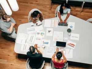 Five people gathered around a table reviewing charts and graphs, some using laptops.