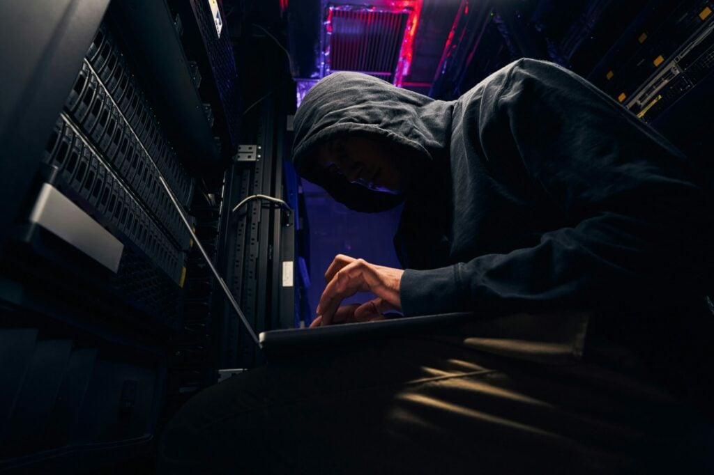 In a dimly lit server room, a person in a hoodie works diligently on a laptop, crafting an effective cybersecurity strategy.