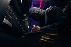 In a dimly lit server room, a person in a hoodie works diligently on a laptop, crafting an effective cybersecurity strategy.