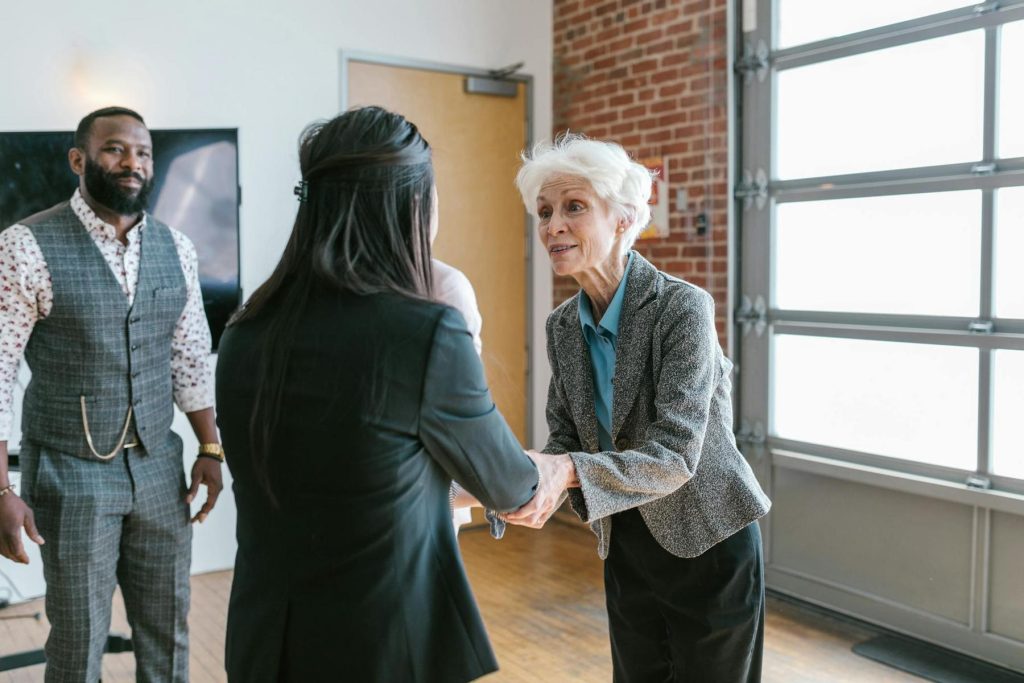 Three people in a modern office space, two women are shaking hands, while a man stands nearby observing.